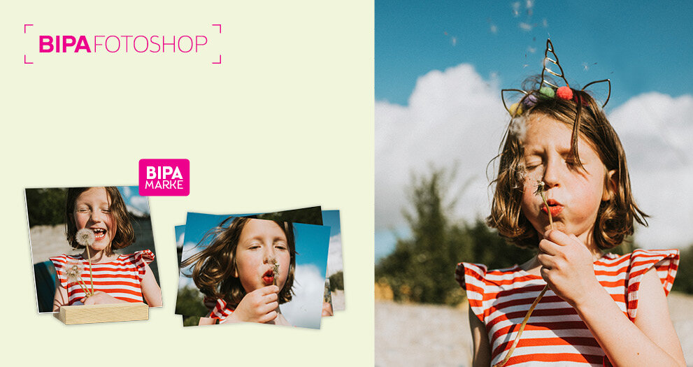 Mädchen bläst Pusteblume im Sonnenschein, links BIPA Fotoshop Abzüge und Fotohalter mit fröhlichem Frühlingsmotiv.